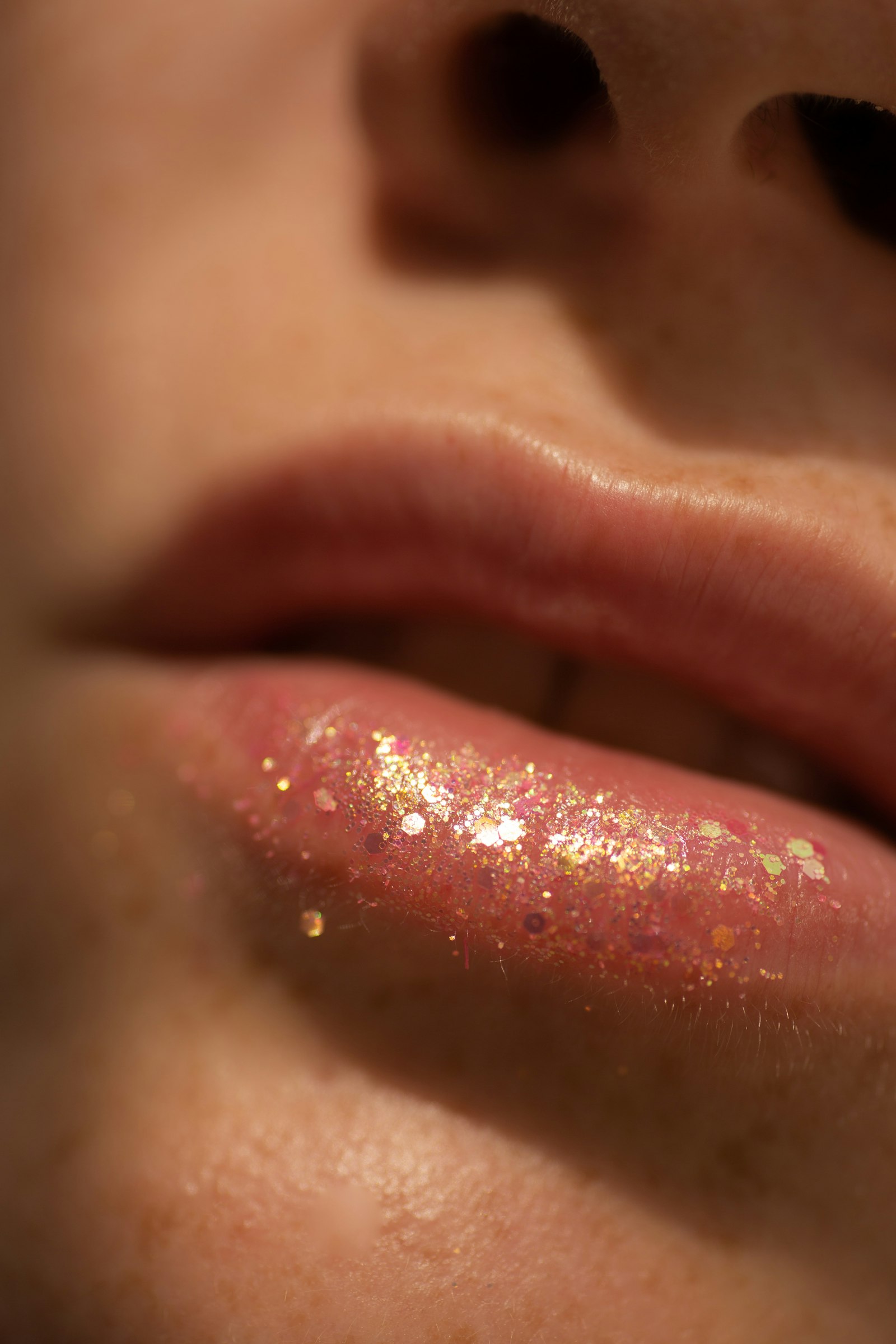 Extreme close-up of lips wearing pink lip gloss packed with gold and iridescent glitter