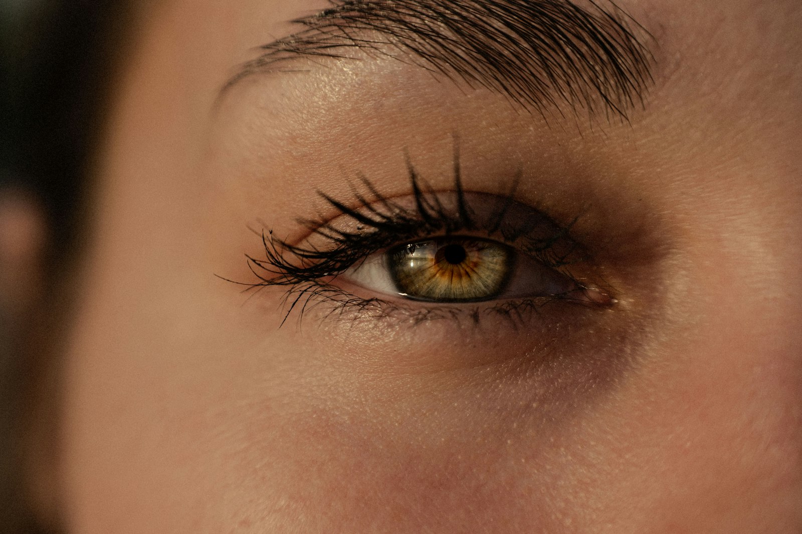 Warm-lit close-up of a hazel-green eye with long dark lashes and a natural brow