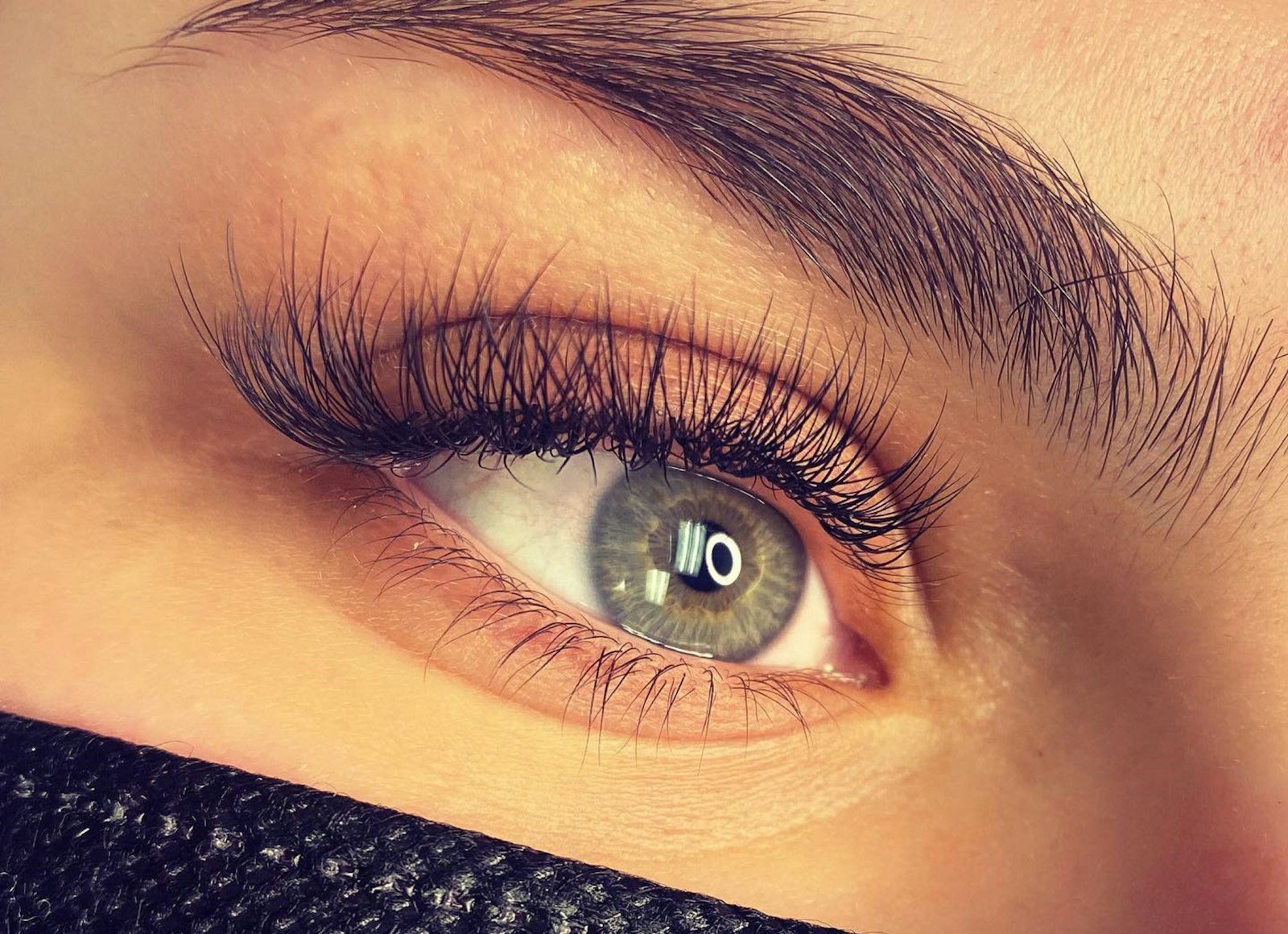 Close-up of an open green eye with long fanned volume lash extensions and a full brushed-up brow