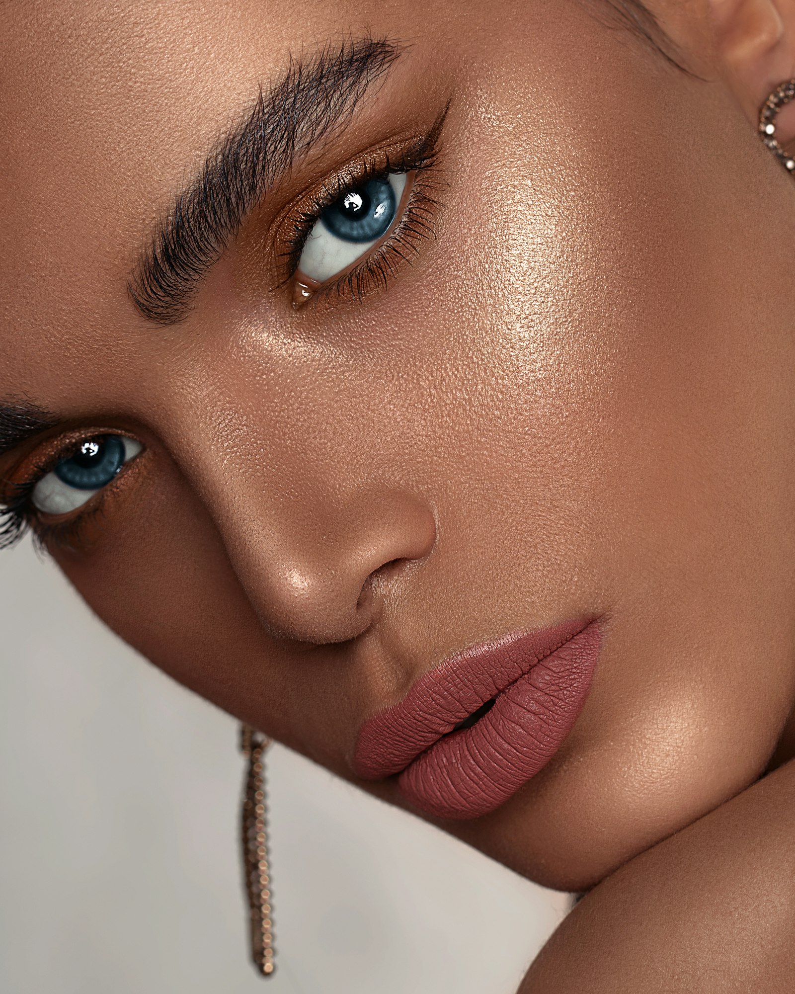 Beauty portrait of a model with glowing skin, bold brows, bronze eyeshadow and rose lips