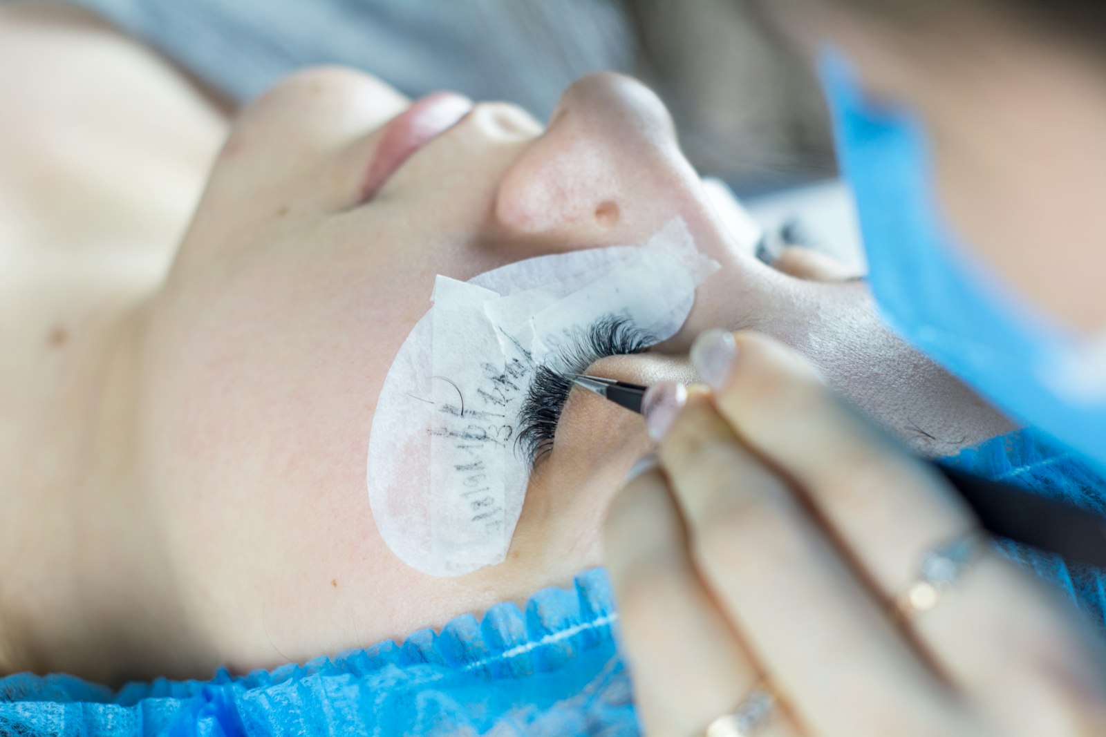 A lash artist applying extensions with tweezers to a reclined client wearing under-eye gel pads