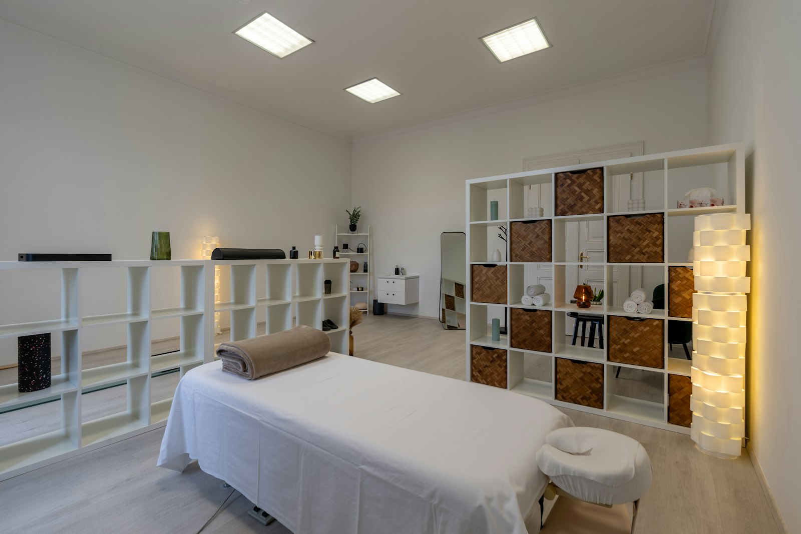 A made-up treatment bed with folded towels and white shelving in a bright treatment room