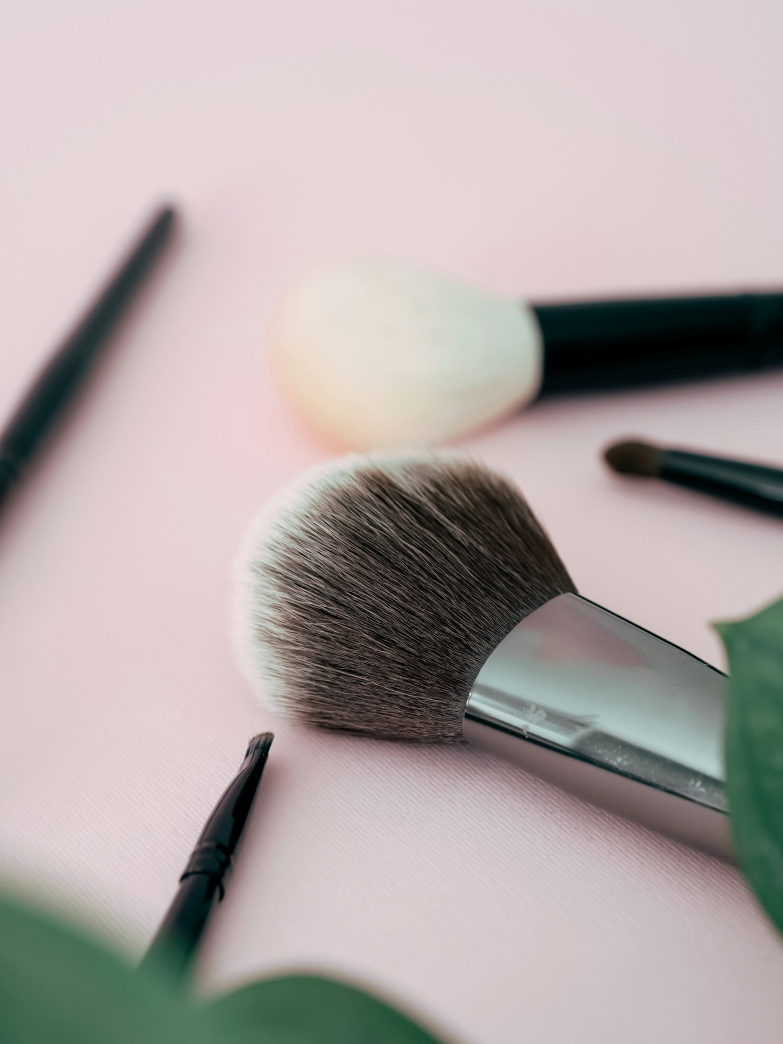 Makeup brushes and brow pencils laid out on a pale pink surface