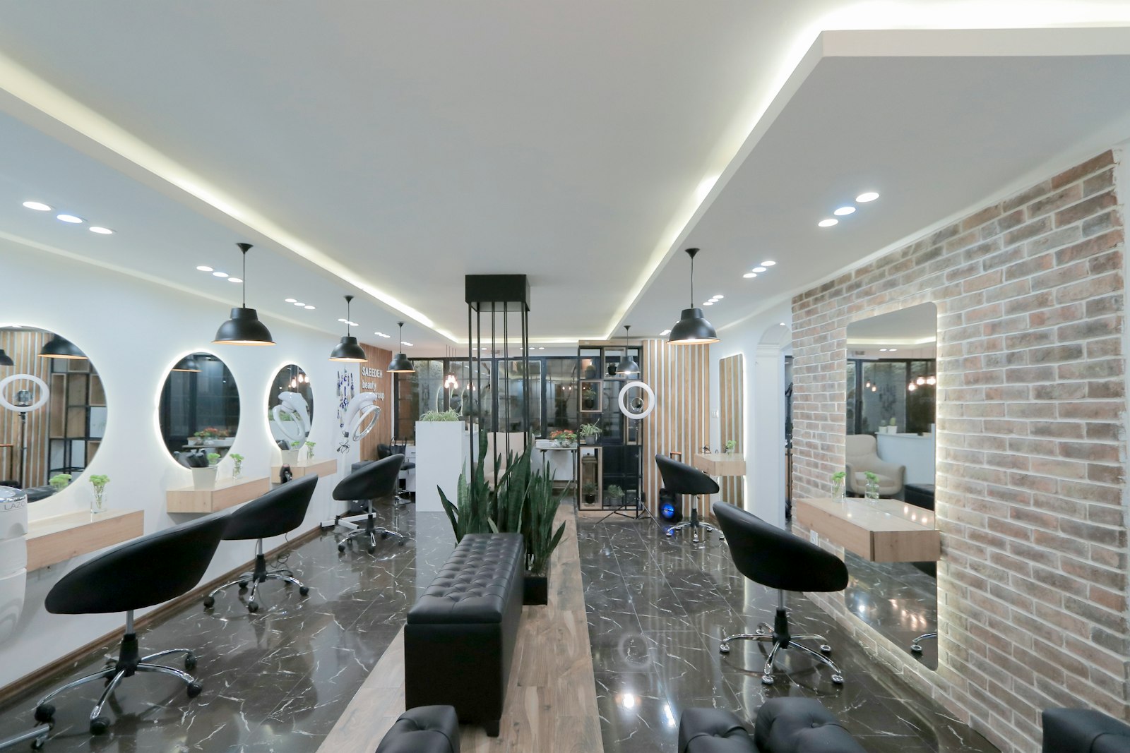 Row of round backlit mirrors and black chairs along an exposed brick wall in the studio